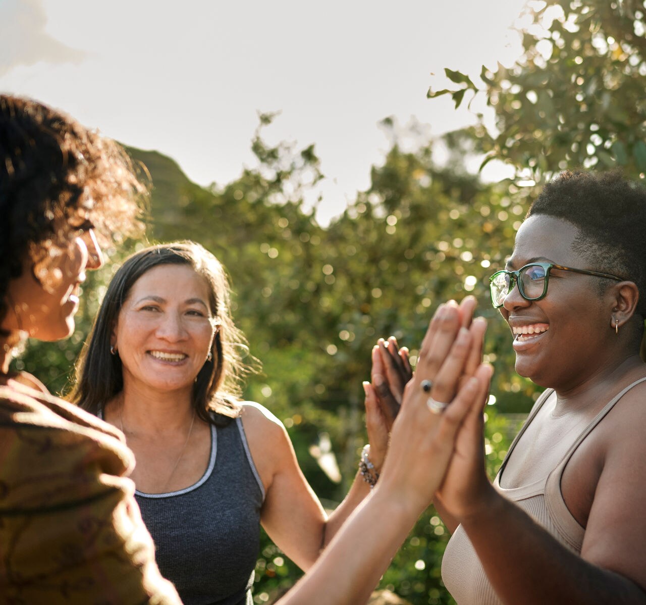 Laughing woman and a group of other women standing with her hands together during an exercise at a wellness retreat in summer